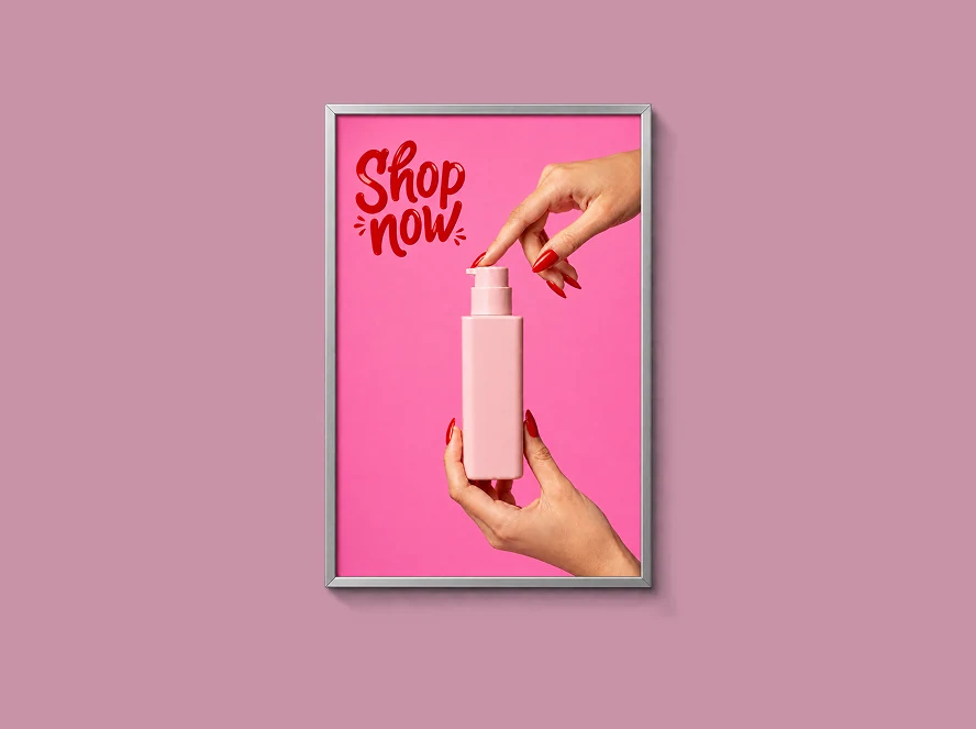 Framed pink advertisement with Shop now lettering and hands holding a pump bottle on a dusty pink background.